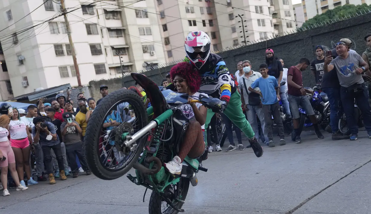 Seorang pengendara sepeda motor bersama seorang penumpang melakukan wheelie di atas sepeda motornya saat pameran di kawasan El Valle, Caracas, Venezuela, Sabtu (31/7/2021). (AP Photo/Ariana Cubillos)