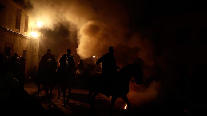 Orang-orang menunggangi kuda melewati api unggun saat festival Luminarias di San Bartolome de Pinares, Spanyol, Jumat (16/1/2020). Setelah api dari tumpukan kayu bakar telah siap, para penunggang kuda mengantri bersiap untuk menembus kobaran api tersebut. (AP Photo/Manu Fernandez)