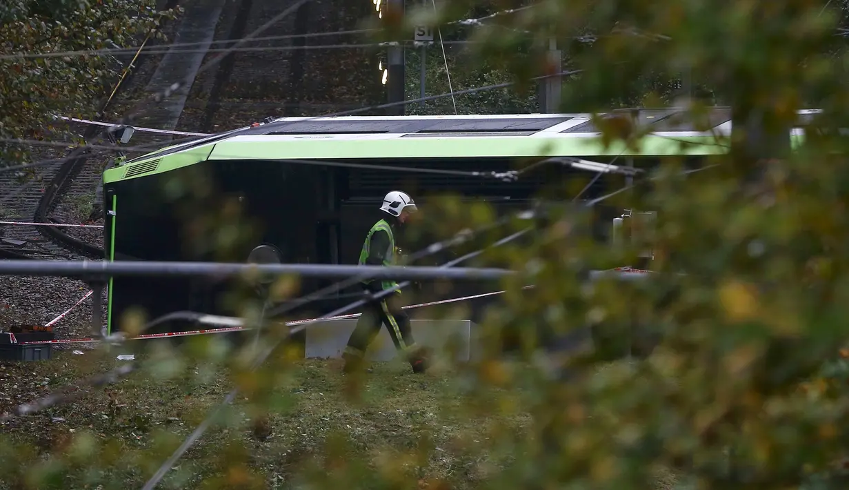 Petugas layanan darurat berjalan melewati sebuah trem yang terbalik di Croydon, London Selatan, Inggris, Rabu (9/11). Pihak berwajib telah mengamankan pengemudi trem asal Beckenham yang diduga lalai sehingga menyebabkan kematian. (REUTERS/Neil Hall)