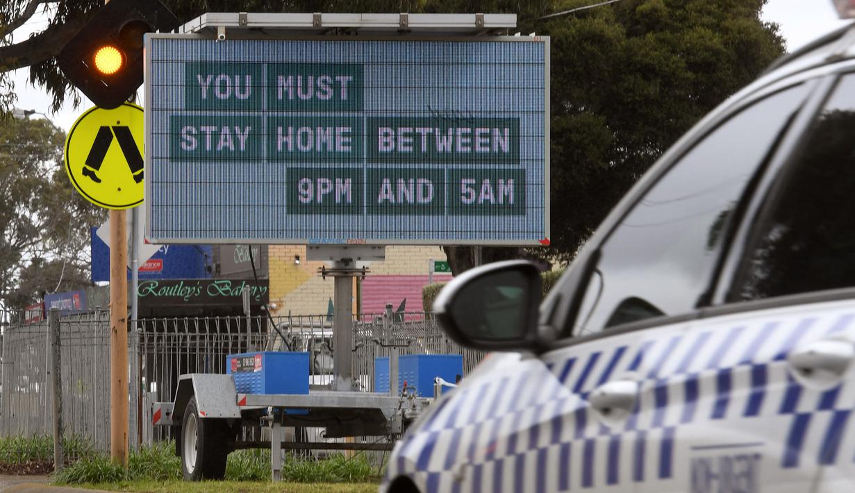 Sebuah mobil polisi melewati tanda jam malam saat kota itu mengalami penguncian keenam saat memerangi wabah varian Delta dari coronavirus.di Melbourne (25/8/2021). (AFP/William West)