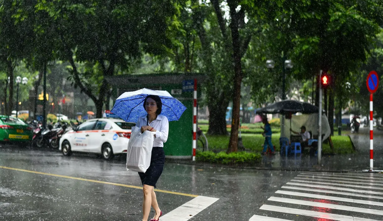 Seorang wanita melintasi jalan saat hujan lebat di Hanoi (14/10/2020). Badai tropis Nangka menghantam Vietnam tengah-utara yang mengakibatkan bencana alam, terutama hujan lebat dan banjir, telah menyebabkan 28 orang tewas dan 12 lainnya hilang. (AFP Photo/Manan Vatsyayana)