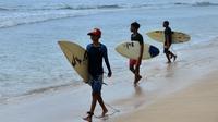 Anak-anak berjalan dengan papan selancar mereka di pantai Kuta di pulau resor Bali (4/10/2021). Pemerintah melonggarkan secara bertahap PPKM berjenjang dengan membuka Bandara Internasional Ngurah Rai untuk kedatangan internasional mulai 14 Oktober. (AFP/Sony Tumbelaka)