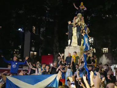 Suporter Skotlandia berkumpul dan merayakan keberhasilan negaranya menahan imbang Inggris pada laga Euro 2020 di patung William Shakespeare di Leicester Square, London, Jumat (18/6/2021). (AP/Kirsty Wigglesworth)
