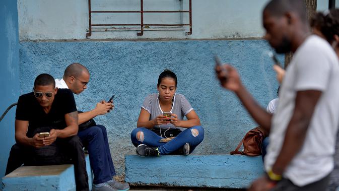 Orang-orang menggunakan ponsel mereka untuk terhubung ke internet melalui WiFi di sebuah taman di Havana, Rabu (5/12). Pemerintah Kuba mengumumkan bahwa masyarakat bisa mengakses internet secara bebas di ponsel mereka mulai Kamis ini. (YAMIL LAGE/AFP)
