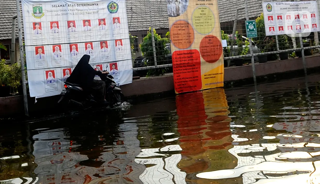 Guru melewati banjir yang menggenangi halaman  sekolah di SMAN 4 Tangsel, Pondok Ranji, Tangerang Selatan, Banten, Selasa (14/6/2022). Tiga  pekan lebih banjir merendam lapangan sekolah itu dikarenakan tertutupnya saluran air oleh sampah yang berasal dari tempat pembuangan sampah (TPS) ilegal. (merdeka.com/Arie Basuki)