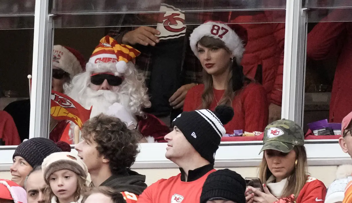 Taylor Swift (kanan) duduk di samping kakaknya, Austin yang berdandan ala Santa Klaus saat menyaksikan pertandingan NFL (National Football League) antara Kansas City Chiefs melawan Las Vegas Raiders di Arrowhead Stadium, Kansas, Amerika Serikat, Selasa (26/12/2023) WIB. (AP Photo/Charlie Riedel)