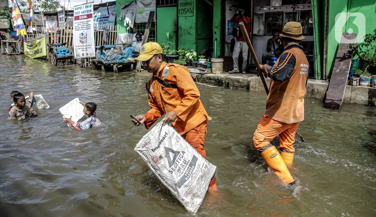 Petugas PPSU membersihkan sampah saat terjadi banjir rob di Pelabuhan Kali Adem, Muara Angke, Jakarta, Selasa (9/11/2021). Walau terendam banjir rob, petugas PPSU tetap sigap bersihkan sampah yang mengambang terbawa air laut. (Liputan6.com/Faizal Fanani)