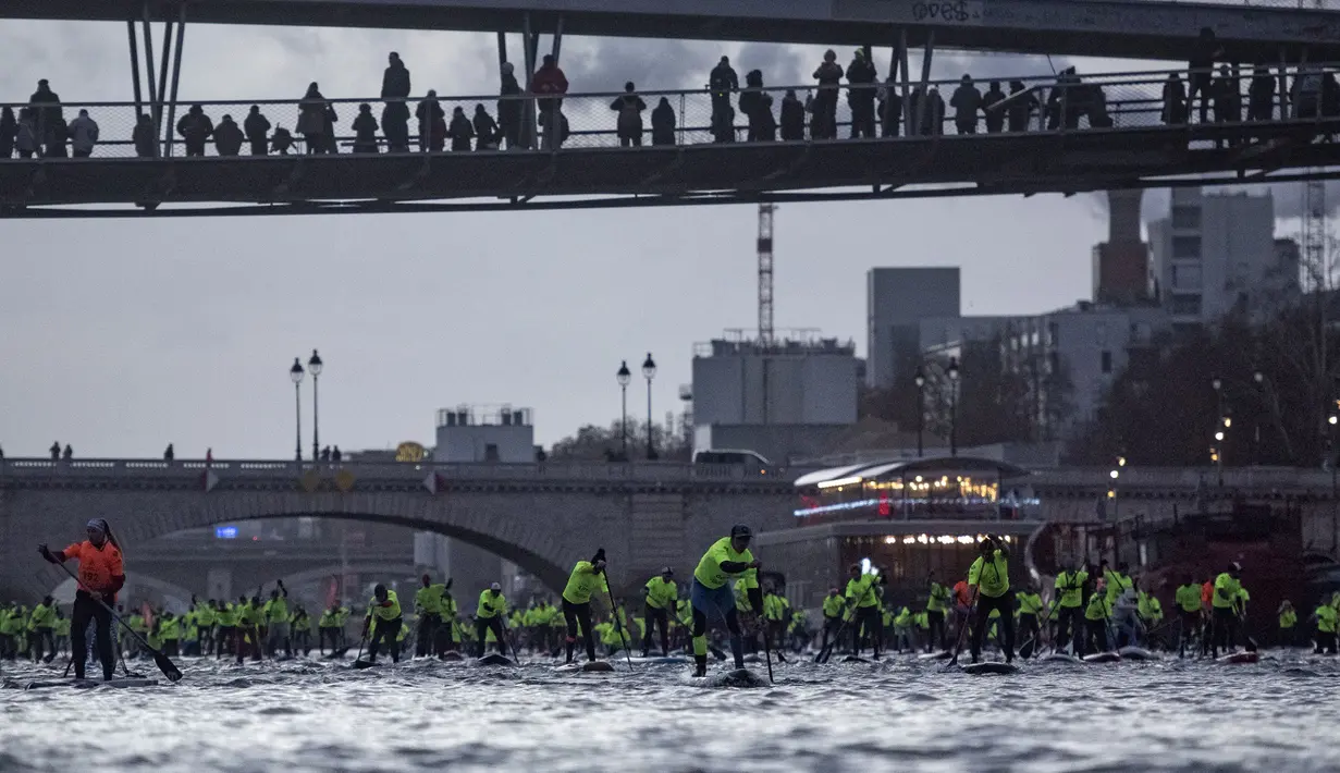 Para peserta mengambil bagian dalam Nautic Paddle Race di Paris, Minggu (9/12). Sekitar 800 orang mengikuti lomba dayung sambil berdiri terbesar di dunia sejauh 11 km menyeberangi sungai Seine. (Lucas BARIOULET/AFP)