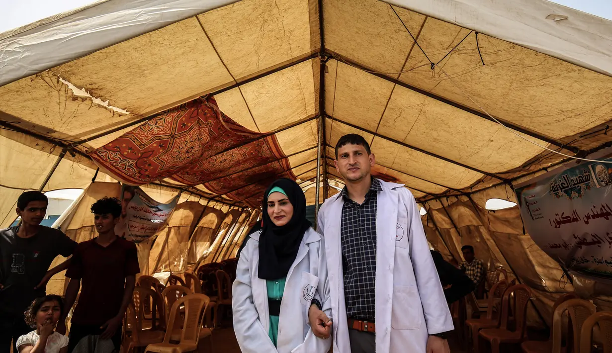 Pasangan petugas medis Muadh Al-Raqab (kanan) dan Hadeel Al-Najjar yang baru menikah berfoto di luar tenda di jalur Gaza selatan, Palestina (2/5). Petugas medis ini harus melangsungkan pernikahannya di dalam tenda. (AFP Photo/Said Khatib)