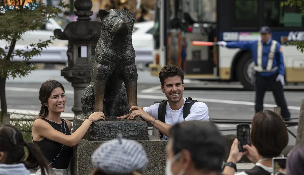 Pasangan berpose untuk berfoto di samping patung "Hachiko" di depan stasiun Shibuya di pusat kota Tokyo menjelang peringatan 100 tahun kelahiran anjing legendaris tersebut bulan ini pada 6 November 2023. (Richard A. Brooks / AFP)