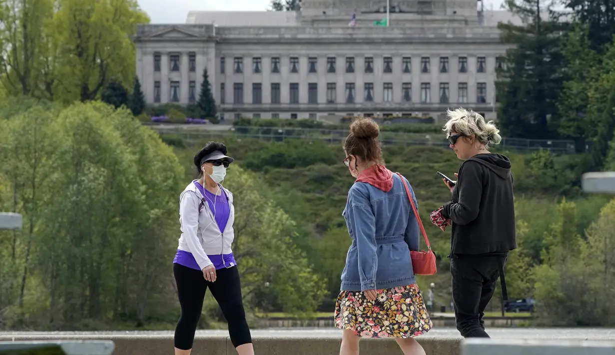 Pejalan kaki dengan masker dan tanpa masker berjalan di dekat Capitol di Olympia, Washington, Selasa (27/4/2021). Warga Amerika Serikat (AS) yang telah menerima vaksin COVID-19 tidak lagi diwajibkan mengenakan masker saat berada di luar ruangan jika tidak ada kerumuman. (AP Photo/Ted S. Warren)