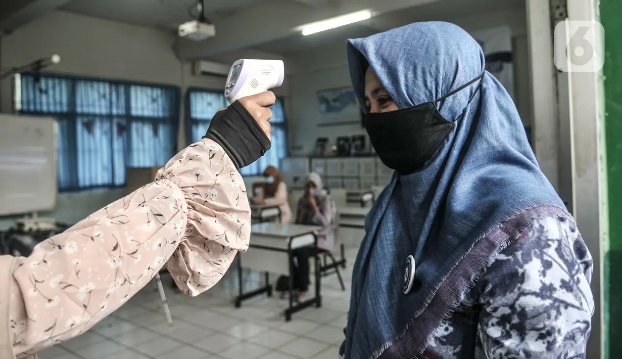Guru diperiksa suhu sebelum memasuki ruang kelas saat sekolah dengan model Kelas Hybrid di SMPN 255, Jakarta, Selasa (30/3/2021). Simulasi kegiatan belajar mengajar (KBM) dengan model kelas Hybrid digelar terkait rencana sekolah tatap muka di awal tahun ajaran baru. (merdeka.com/Iqbal S Nugroho)