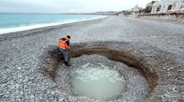 Seorang pria turun melihat kawah misterius berisi air payau yang muncul di Pantai Lido, Nice, Prancis, Kamis (1/2). Lubang selebar 5 meter dan sedalam 2 meter itu membuat banyak warga sekitar kebingungan. (VALERY HACHE/AFP)