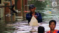 Petugas Sudin Sumber Daya Air (SDA) memunguti sampah-sampah yang tergenang saat banjir di kawasan Kampung Melayu Kecil, Bukit Duri, Jakarta, Selasa (25/2/2020). Banjir tersebut akibat luapan sungai Ciliwung. (merdeka.com/magang/ Muhammad Fayyadh)