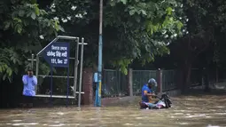 Pengendara motor  berdiri di jalan yang tergenang air setelah hujan monsun di Gurgaon di pinggiran New Delhi (19/8/2020). Jumlah korban dari banjir tahunan di seluruh Asia Selatan naik menjadi hampir 1.300. (AFP/Xavier Galiana)