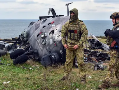 Tentara Ukraina berdiri dengan latar belakang helikopter militer Rusia yang rusak di Pulau Ular, Laut Hitam, Ukraina, 18 Desember 2022. Pasukan Rusia menduduki pulau itu pada awal-awal invasinya ke Ukraina, namun akhirnya mundur beberapa bulan kemudian. (AP Photo/Michael Shtekel)