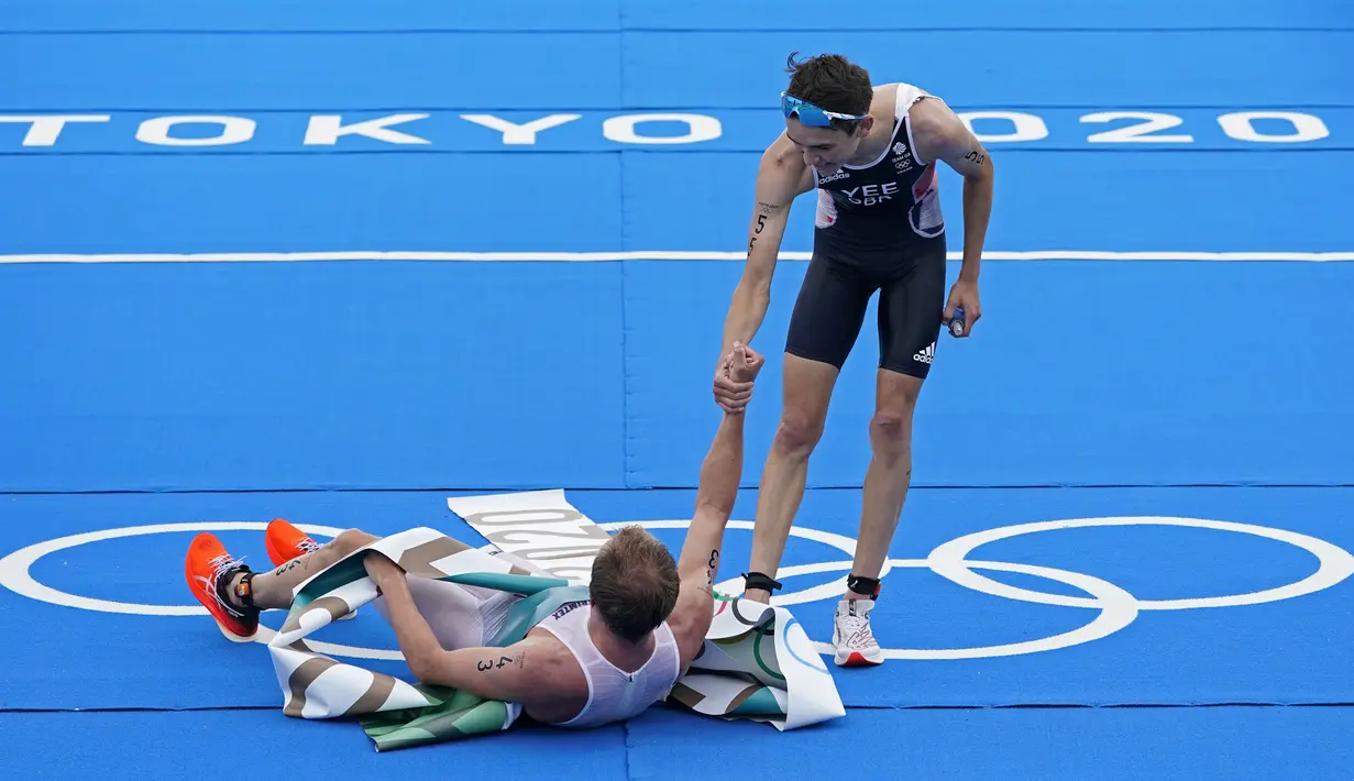 Atlet Inggris Alex Yee (55) mengulurkan tangan untuk membantu atlet Norwegia Kristian Blummenfelt (43) setelah Blummenfelt memenangkan medali emas dan Yee memenangkan perak pada triathlon individu putra Olimpiade Tokyo 2020 di Tokyo, Jepang, 26 Juli 2021. (AP Photo/David Goldman)