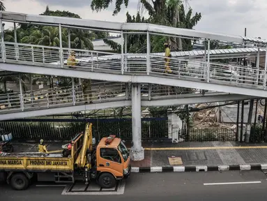 Petugas Sudin Bina Marga Jakarta Timur memperbaiki jembatan penyeberangan orang (JPO) di Jalan Otto Iskandardinata (Otista), Jatinegara, Rabu (9/2/2022). Perbaikan JPO itu tindak lanjut pasca insiden tertimpa pohon tumbang pada November tahun lalu akibat cuaca ekstrem. (merdeka.com/Iqbal S Nugroho)