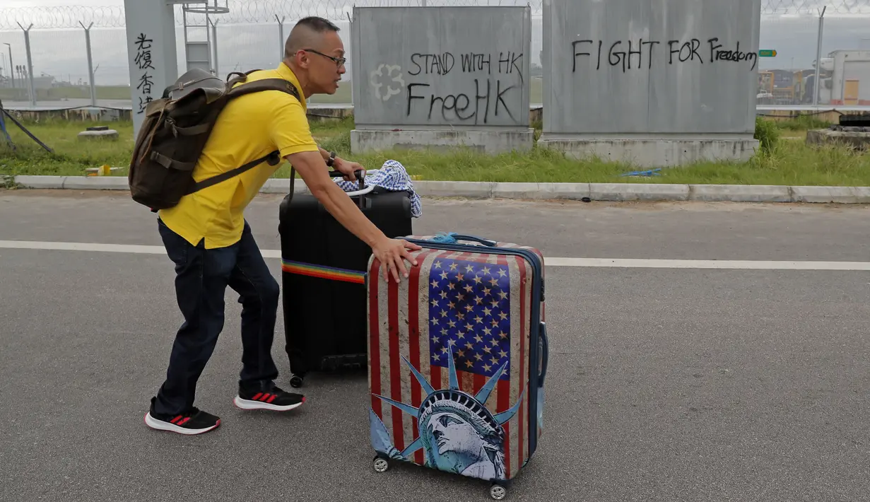 Seorang penumpang membawa koper berjalan kaki ke bandara ketika pemrotes pro-demokrasi memblokir jalan di luar bandara di Hong Kong (1/9/2019). Akibat pemblokiran jalan dan layanan kereta api para calon penumpang pesawat terpaksa berjalan kaki menuju bandara. (AP Photo/Kin Cheung)