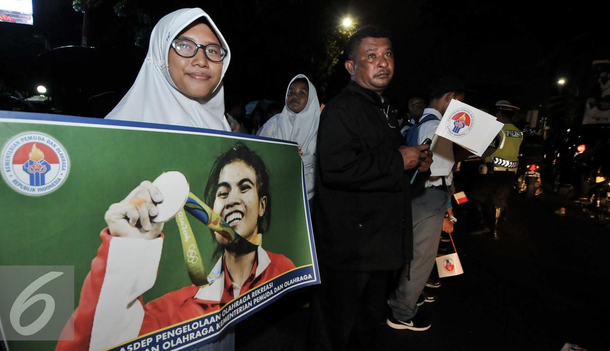 Seorang wanita membentangkan spanduk dengan gambar Sri Wahyuni peraih medali perak di Olimpiade Rio 2016, Jakarta, Selasa (23/8). Warga menyambut antusias kedatangan para atlet yang berlaga di Olimpiade Rio 2016. (Liputan6.com/Yoppy Renato)