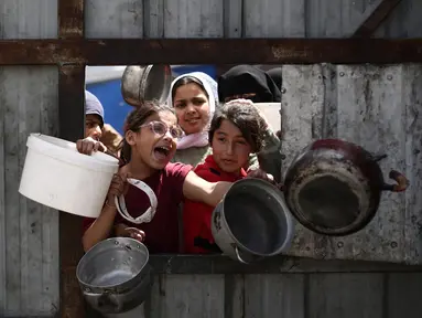 Anak-anak Palestina memberi isyarat saat mereka mengantre untuk mengambil makanan di titik distribusi makanan gratis di kamp pengungsi Nuseirat, Jalur Gaza tengah, pada 3 April 2025. (Eyad BABA/AFP)