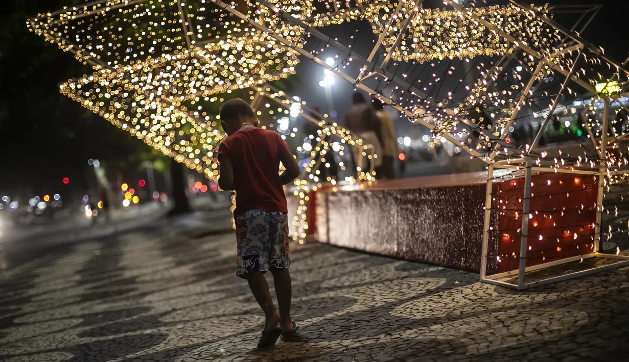 Seorang anak berjalan di sepanjang trotoar pantai Copacabana dengan latar belakang lampu Natal, di Rio de Janeiro, Brasil (11/12/2021). Jelang perayaan Natal, taman dan pantai dihiasi lampu-lampu yang indah. (AP Photo/Bruna Prado)