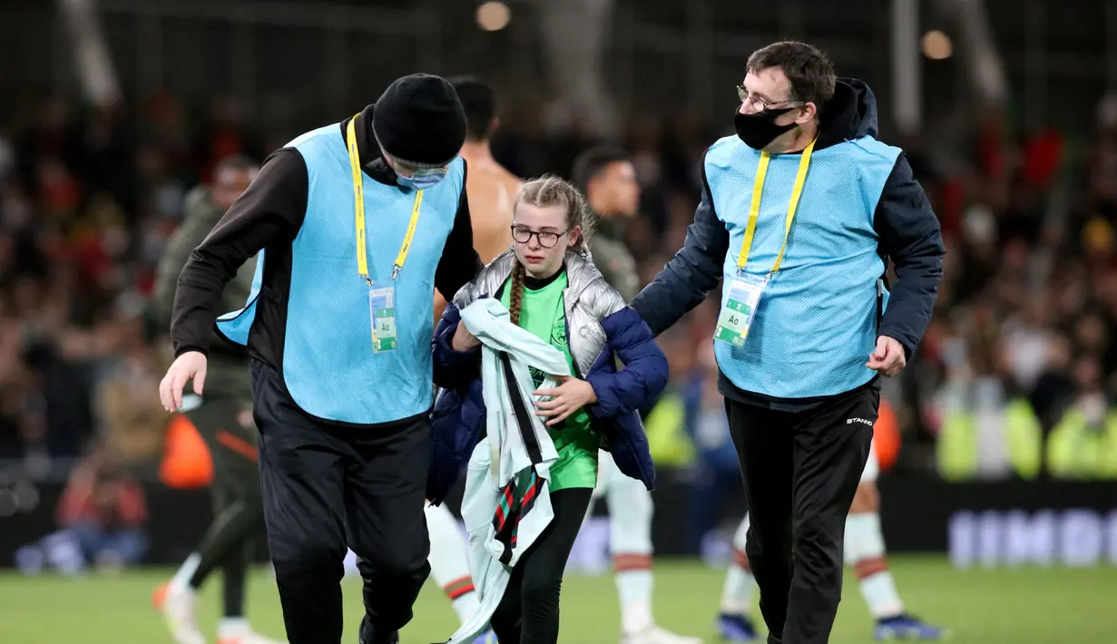 Seorang fans cilik memegang jersey striker Portugal Cristiano Ronaldo (tidak terlihat) saat dikawal keluar lapangan oleh petugas setelah menerobos masuk pada akhir laga Grup A Kualifikasi Piala Dunia 2022 Zona Eropa melawan Irlandia di Stadion Aviva, Jumat (12/11/2021) dinihari WIB. (Paul Faith / AF