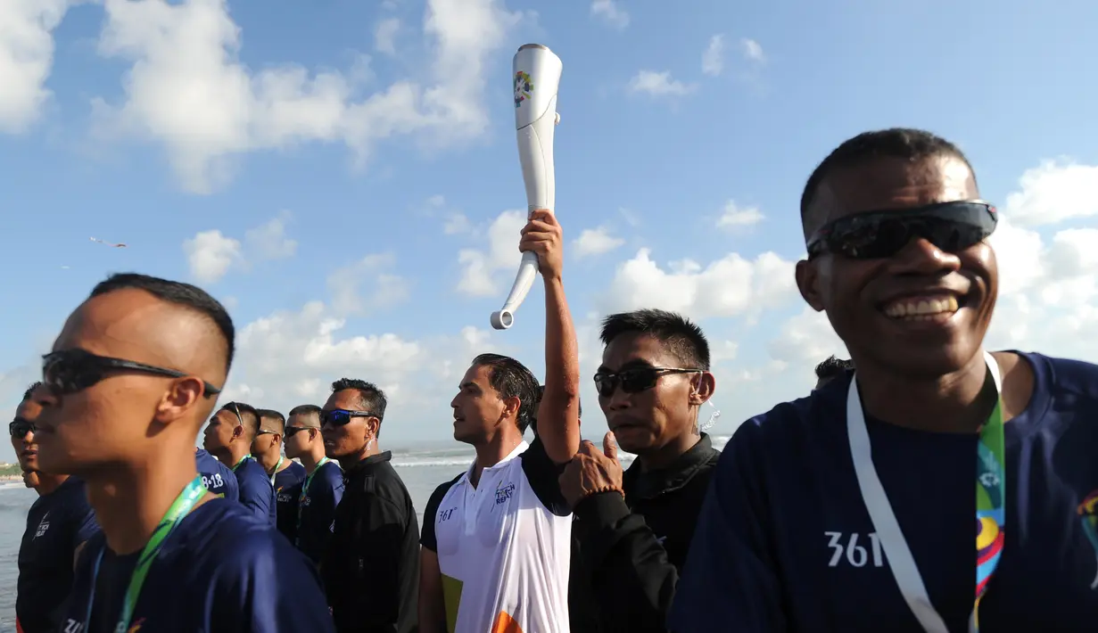 Aktor Hamish Daud (tengah) membawa obor pada kirab obor Asian Games 2018 di Pantai Kuta, Bali, Senin (23/7). Hamish menerima obor yang diserahkan oleh Menko Bidang Pembangunan Manusia dan Kebudayaan, Puan Maharani. (AFP/SONNY TUMBELAKA)