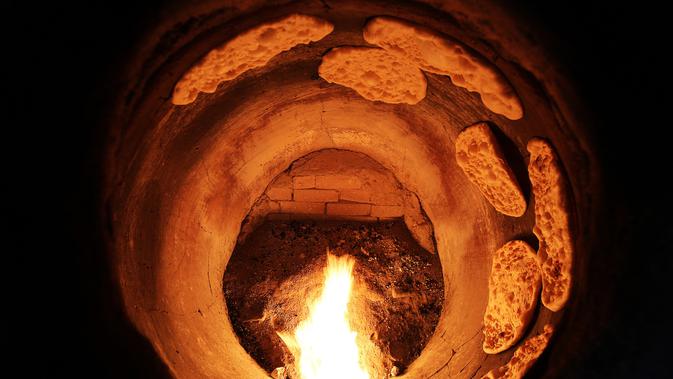 Proses pemanggangan roti Iran atau taftoon dalam oven tradisional di sebuah toko di Kuwait City, Kuwait, 27 Juni 2019. Taftoon telah menjadi makanan pokok untuk sarapan, makan siang, dan selalu menghiasi meja makan orang Kuwait selama beberapa dekade. (YASSER AL-ZAYYAT/AFP)