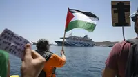 Seorang pengunjuk rasa mengibarkan bendera Palestina saat massa melakukan unjuk rasa di depan kapal pesiar yang membawa turis asal Israel dan berusaha mendekati Pulau Syros di Laut Aegea, Yunani, pada Selasa (22/7/2025). (Dok. Nikos Panagiotopoulos/InTime News via AP)&nbsp;