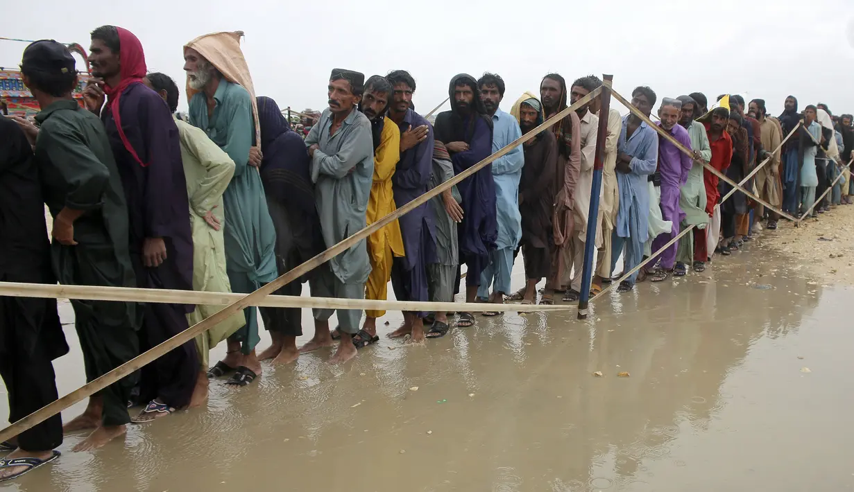 Pengungsi menunggu giliran untuk mendapatkan makanan dan barang-barang lainnya yang dibagikan oleh tentara di sebuah kamp bantuan di daerah yang dilanda banjir di distrik Jamshoro, di Pakistan selatan, Rabu (24/8/2022). Hujan deras telah memicu banjir bandang dan mendatangkan malapetaka di banyak tempat. (AP Photo/Pervez Masih)