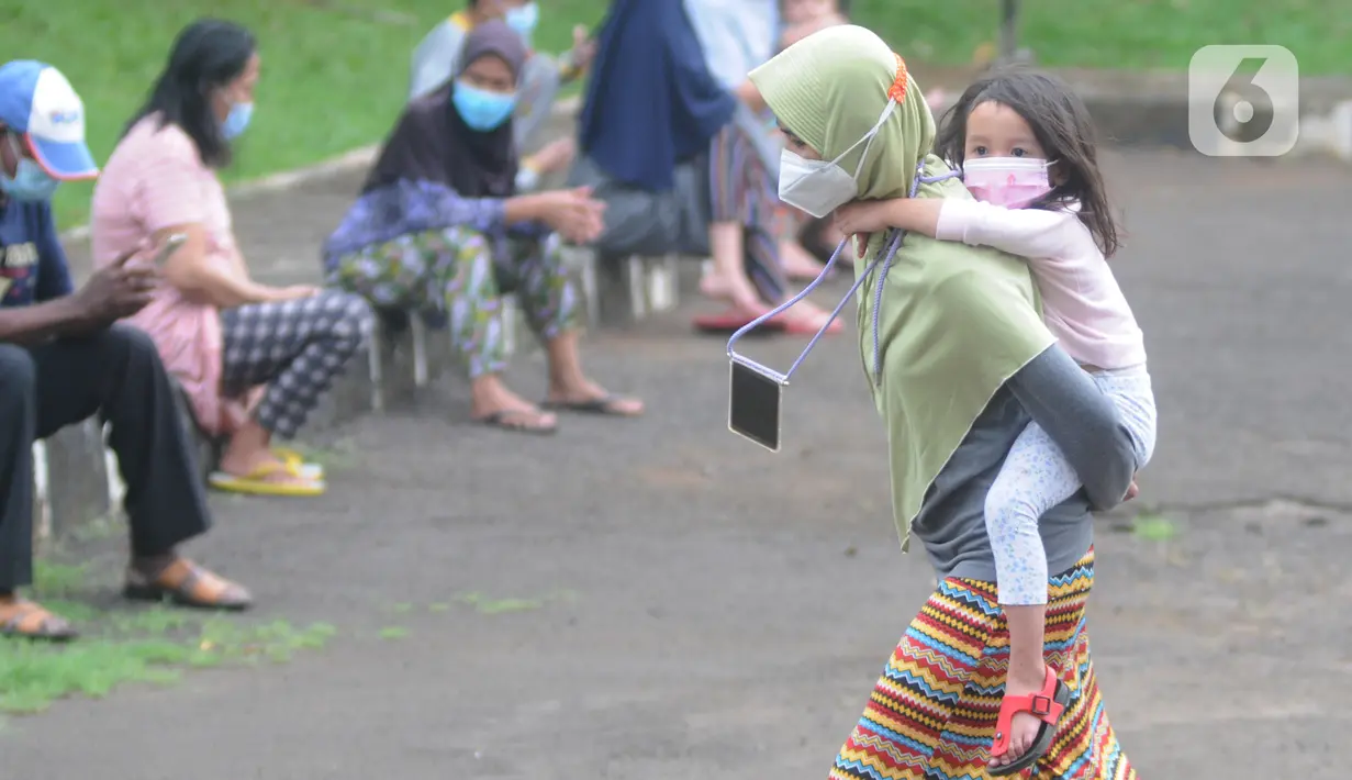 Pasien Covid-19 menggendong seorang anak melintas di halaman Graha Wisata Ragunan, Jakarta, Selasa (15/6/2021). Pemprov DKI memfungsikan kembali Graha Wisata Ragunan sebagai tempat isolasi warga terpapar COVID-19 kategori OTG sejak pekan lalu dan saat ini merawat 117 pasien (merdeka.com/Arie Basuki)
