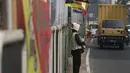 Pedagang berdiri dekat bendera negara peserta Asian Games 2018 di pagar pembatas Jalan Pluit Selatan Raya, Jakarta, Kamis (19/7). Pemasangan bendera bertiangkan bambu itu dianggap justru dapat mempermalukan Indonesia. (Liputan6.com/Arya Manggala)