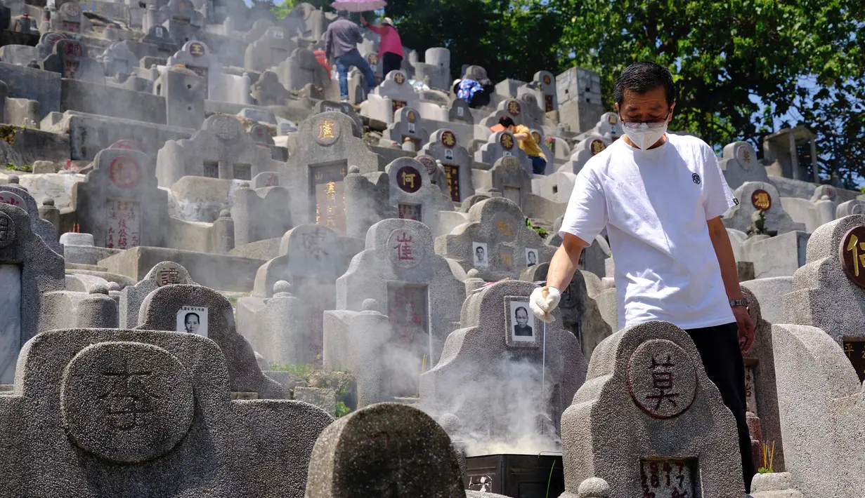 Seorang pria yang mengenakan masker membakar uang kertas di makam kerabat saat Festival Ching Ming atau Hari Sapu Makam di Hong Kong, Selasa (5/4/2022). Ribuan warga Hong Kong memberi hormat kepada leluhur dan kerabat mereka selama festival tahunan ini. (AP Photo/Vincent Yu)