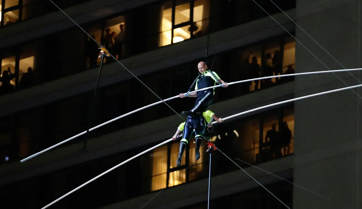 Aerialists Nik Wallenda (atas) melangkahi saudara perempuannya Lijana Wallenda saat melintasi seutas kawat di ketinggian 396 meter, Times Square, New York, AS, Minggu (23/6/2019). Nik dan Lijana berjalan dari sisi berbeda yang digantung di antara dua menara Times Square. (AP Photo/Jason Szenes)