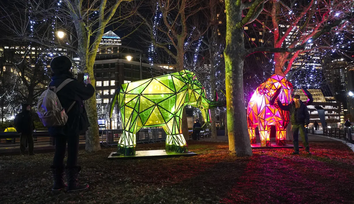Orang-orang memotret "Permafrost - Sleeping Giants" karya Fisheye, sebagai bagian dari festival Winter Lights di Canary Wharf, di London, Rabu (18/1/2023). Festival ini menerangi Canary Wharf dengan koleksi spektakuler lebih dari 20 instalasi. (AP Photo/Alberto Pezzali)