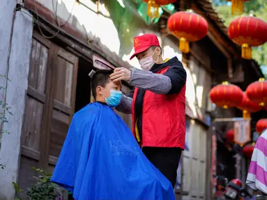 Seorang barber sukarelawan memotong rambut seorang anak laki-laki di sebuah permukiman di Kota Chongqing, China, pada 16 Februari 2020. Sejak merebaknya virus corona COVID-19, sebagian besar tempat potong rambut telah ditutup. (Xinhua/Liu Chan)