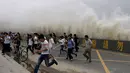 Wisatawan berlari saat gelombang air pasang tinggi melewati penghalang di tepi Sungai Qiantang di Hangzhou, provinsi Zhejiang, Tiongkok, 4 Oktober 2016. Hantaman gelombang ini menjadi daya tarik tersendiri bagi wisatawan. (REUTERS)