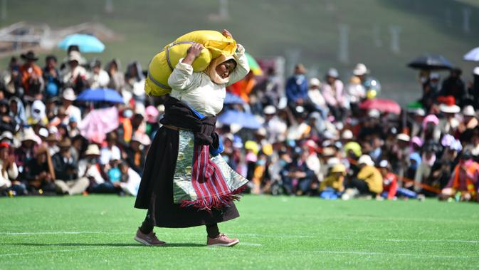 Seorang partisipan mengangkat karung berisi barli dataran tinggi dalam sebuah kompetisi yang digelar saat festival balap kuda Dangjiren di Wilayah Damxung, Daerah Otonom Tibet, China barat daya, pada 11 Agustus 2020. (Xinhua/Jigme Dorje)