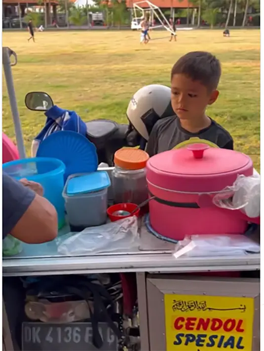 Presenter yang juga pemeran yang beberapa tahun belakangan ini menetap di Bali, membagikan beberapa video singkat putranya jajan makanan kaki lima. Potret El Barack saat jajan es cendol di pinggir lapangan sepak bola. [Instagram/inijedar]