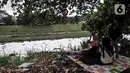 Warga bersantai di dekat limbah busa yang memenuhi aliran Kanal Banjir Timur (KBT), Duren Sawit, Jakarta, Kamis (2/7/2020). Busa yang memenuhi aliran KBT akibat limbah pabrik dan rumah tangga sejak dua minggu lalu itu menjadi tontonan warga meski menimbulkan bau tak sedap (merdeka.com/Iqbal Nugroho)