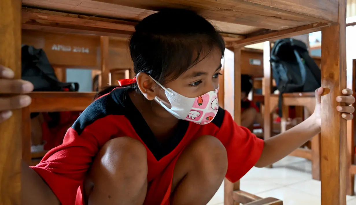 Seorang anak berlindung di bawah meja untuk melindungi dirinya selama latihan gempa dan tsunami di Tanjung Benoa, Kabupaten Badung, Bali, 24 Mei 2022. (SONY TUMBELAKA/AFP)