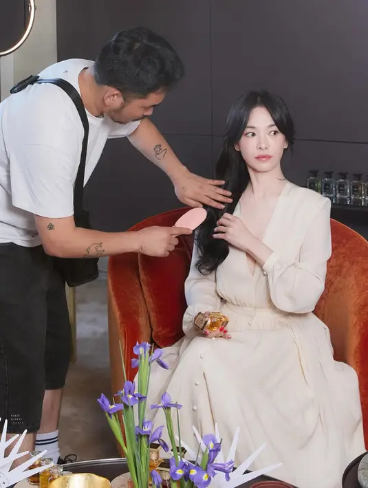 Dalam salah satu momen behind the scenes, Song Hye Kyo terlihat sedang melakukan touch-up rambut sambil memegang botol parfum Guerlain. Rambut hitam panjangnya ditata dalam gelombang lembut yang membingkai wajah, semakin menonjolkan aura klasik yang menjadi ciri khasnya. [Dok/@kyo1122].