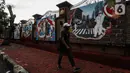 Warga berjalan di samping mural di kawasan Lapangan Bhayangkara, Mabes Polri, Jakarta, selasa (2/11/2021). Selama ini seni mural kurang mendapatkan tempat di fasilitas-fasilitas umum dan Pembuatan Mural ini bagian dalam rangka Bhayangkara Mural Festival 2021. (Liputan6.com/Johan Tallo)
