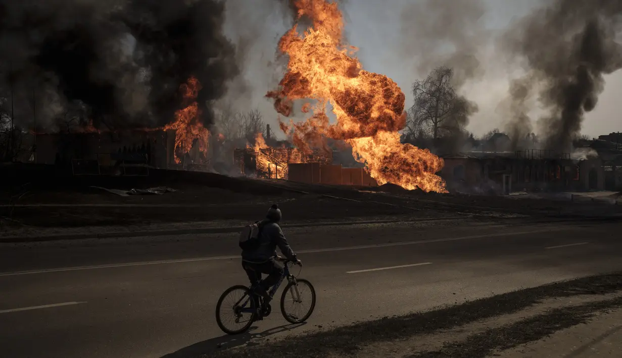 Seorang pria mengendarai sepedanya melewati api dan asap yang mengepul menyusul serangan Rusia di Kharkiv, Ukraina, 25 Maret 2022. (AP Photo/Felipe Dana)