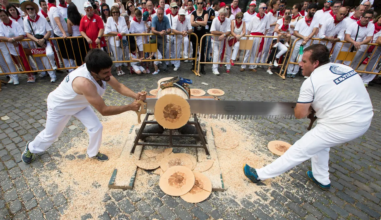 Peserta menggergaji batang pohon dengan "tronza", gergaji tradisional daerah Basque, pada hari ketiga festival San Fermin di Pamplona, Spanyol, Senin (8/7/2019). Festival San Fermin menghadirkan beberapa olahraga pedesaan Basque seperti menggergaji dan memotong pohon dengan kapak. (JAIME REINA/AFP)