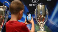Seorang anak laki-laki mengambil foto trofi Piala Super UEFA yang dipajang bersama trofi Liga Champions dan Liga Europa di Palace of Culture and Science di Warsawa, Polandia, pada 8 Agustus 2024. (Sergei GAPON /AFP)