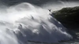 Peselancar mengangkat tangannya saat keluar dari ombak selama sesi selancar derek di Praia do Norte di Nazare, Portugal (29/10/2020). Gelombang besar muncul oleh Badai Epsilon di Atlantik Utara, mencapai pantai barat Portugis menarik peselancar ombak besar ke Nazare. (AP Photo/Pedro Rocha)