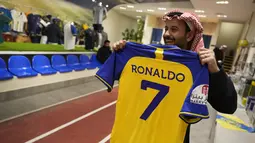Seorang pria memegang kaus Cristiano Ronaldo di toko klub Al Nassr di Riyadh, Arab Saudi, Senin, 2 Januari 2023. Ronaldo menandatangani kontrak dengan Al Nassr dari Arab Saudi pada 31 Desember 2022. Demikian pengumuman klub dalam kesepakatan yang diyakini bernilai lebih dari 200 juta euro. Pemain berusia 37 tahun itu meneken kontrak hingga Juni 2025. (AP Photo/Amr Nabil)