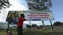 Seorang anak laki-laki berjalan melewati papan reklame dengan pesan dari Presiden Zimbabwe Emmerson Mnangagwa berterima kasih kepada orang-orang karena mengindahkan seruan untuk divaksinasi di Harare, Zimbabwe, Senin (29/11/2021). (AP Photo/Tsvangirayi Mukwazhi)
